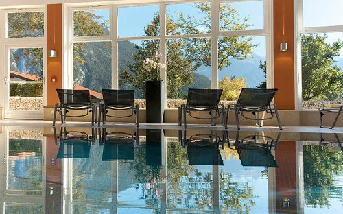 Innenpool mit Liegen und Blick auf Bäume durch große Fenster im Hotel Hirschen.