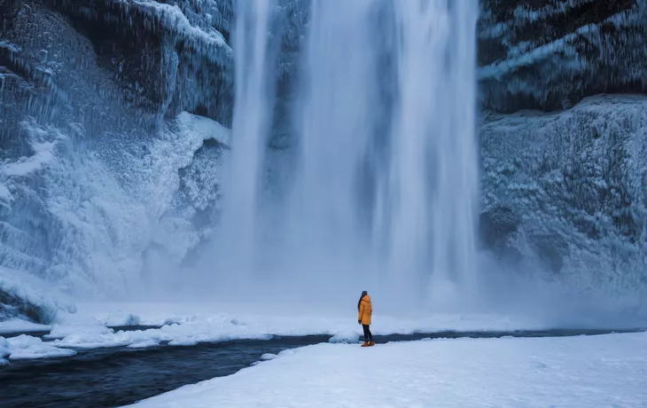 Skogafoss-Wasserfall mit einer einsamen Person, die in der Nähe des Flusses steht