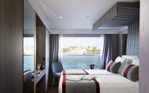 Kabine mit Doppelbett, großem Fenster und Aussicht auf das Wasser.