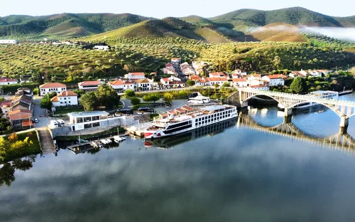 Flusskreuzfahrtschiff am Ufer eines Flusses, Brücke und Hügellandschaft im Hintergrund
