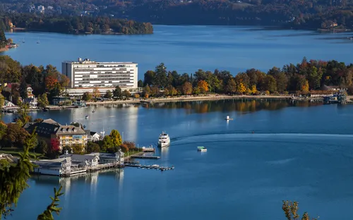 Blick auf einen See mit Hotel und Booten, umgeben von Herbstbäumen.