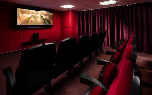Kleiner Kinosaal mit roten Polstersesseln und einer Leinwand an der Wand.