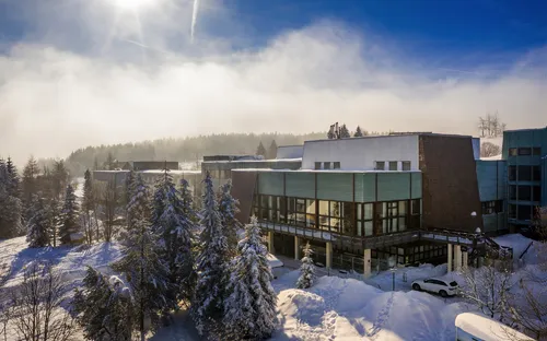 Außenansicht des Ahorn Waldhotels Altenberg im Winter mit Schnee und Bäumen.