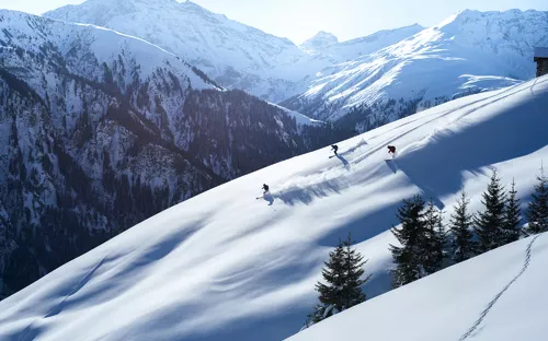 Skifahrer im Pulverschnee auf einem verschneiten Berghang mit Alpenlandschaft im Hintergrund