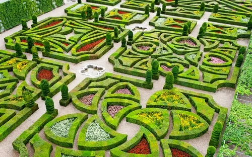 Ornamentaler Garten mit symmetrischen Buchsbaumhecken und bunten Blumeneinfassungen.