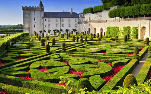 Schloss mit kunstvoll gestaltetem Garten und geschnittenen Hecken im Vordergrund.