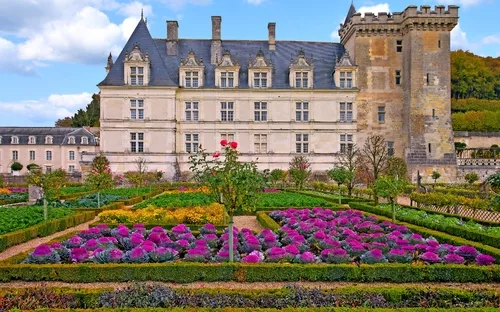 Schloss mit gepflegtem Garten und bunten Blumen im Vordergrund.