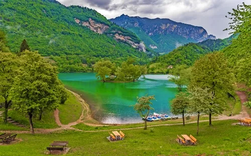 Grüner See inmitten von Bergen, umgeben von Bäumen, mit Booten am Ufer.
