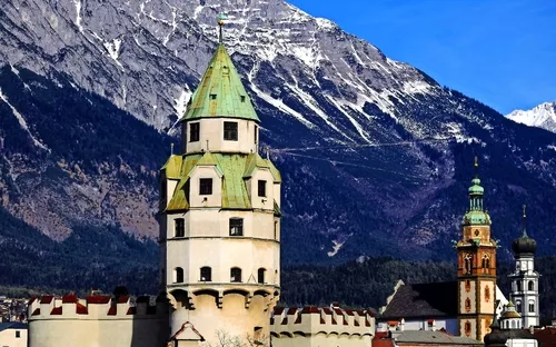 Blick auf einen historischen Turm vor schneebedeckten Bergen bei klarem Himmel.