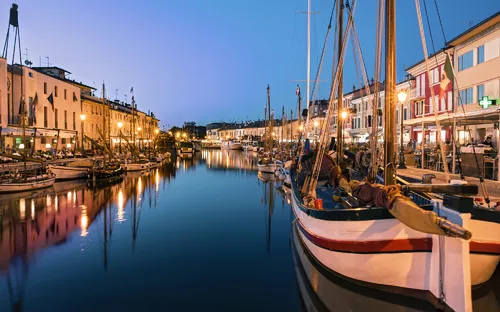 Boote im Hafen bei Abenddämmerung mit beleuchteten Gebäuden im Hintergrund