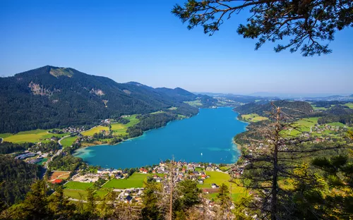 Blick auf einen klaren blauen See inmitten grüner Berge und Dörfer.