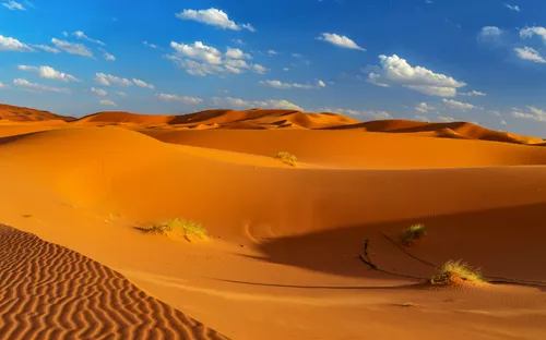 Dünenlandschaft in der Wüste mit blauem Himmel und Wolken.