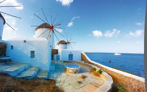 Weißes Gebäude und Windmühlen an der Küste mit blauem Himmel und Meer.