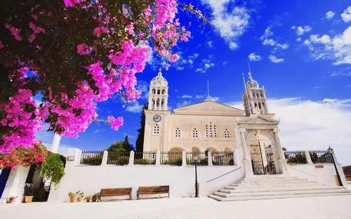 Kirche mit blühendem Baum im Vordergrund und blauem Himmel.