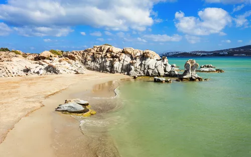 Strand mit Felsenformationen und klarem Wasser unter blauem Himmel mit Wolken.
