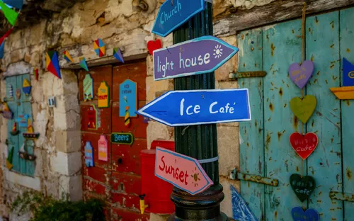 Bunte Schilder an einer Steinwand zeigen in verschiedene Richtungen.