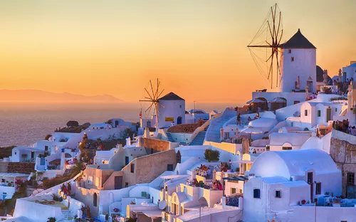 Stadtansicht von Santorini bei Sonnenuntergang mit Windmühlen und weißen Gebäuden.