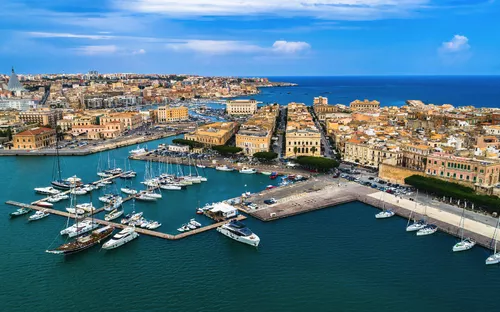 Luftaufnahme eines Hafens mit Yachten und historischen Gebäuden im Hintergrund.