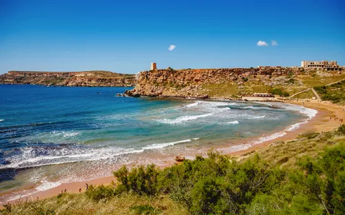 Strand mit Klippen und blauem Meer unter klarem Himmel.