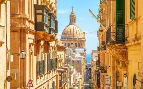Straße in Valletta mit Blick auf eine Kuppel und das Meer im Hintergrund.