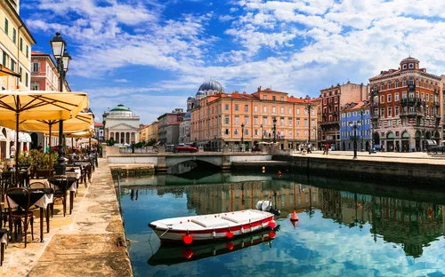Kanal mit Boot, umgeben von historischen Gebäuden und Straßencafés unter blauem Himmel.