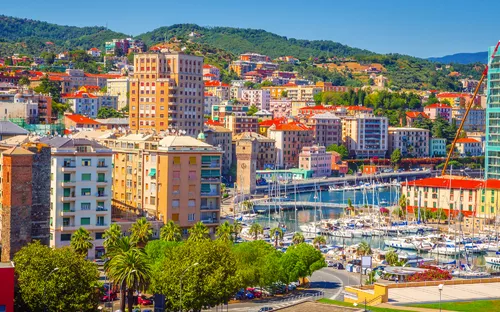 Hafenstadt mit bunten Gebäuden und Segelbooten, umgeben von Hügeln.