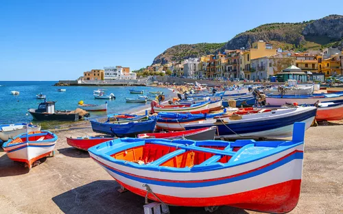 Bunte Boote am Strand, Häuser am Meer und Hügel im Hintergrund.