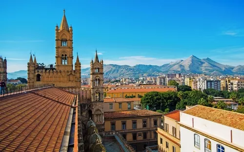 Stadtpanorama mit Kathedrale und Bergen im Hintergrund unter blauem Himmel.