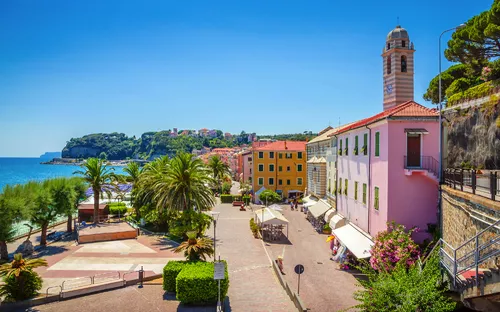 Bunte Häuser an einer Küstenpromenade mit Palmen und Blick aufs Meer.