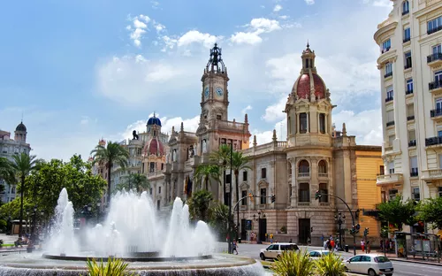 Historisches Gebäude mit Brunnen und Palmen bei Sonnenschein.