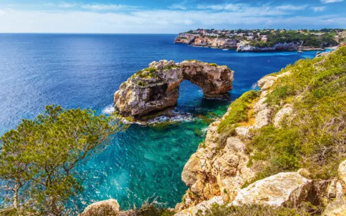 Felsbogen an einer Küste mit blauem Meer und bewachsenem Ufer.