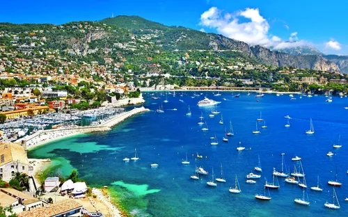 Küstenstadt mit Yachthafen und blauem Meer, gesäumt von Hügeln.