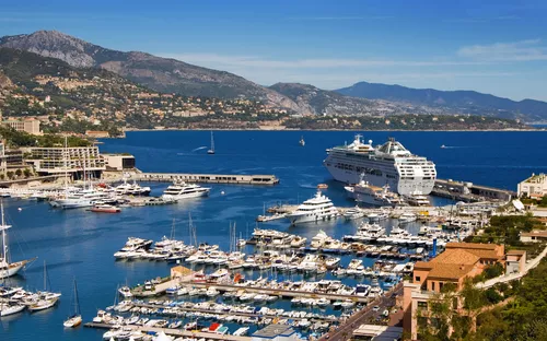 Hafen mit vielen Yachten und einem großen Kreuzfahrtschiff, umgeben von Bergen.