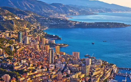 Küstenstadt und umliegende Hügel im Sonnenlicht, mit Blick auf das Meer.