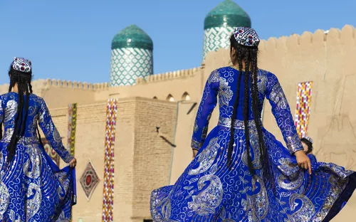 Zwei Frauen in blauen, traditionellen Kleidern vor historischer Architektur.
