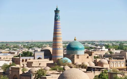 Blick über die Altstadt von Chiwa mit Minarett und Kuppeln im Vordergrund.