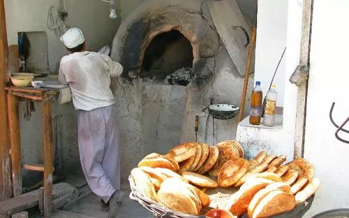 Bäcker am Steinofen mit frischem Brot im Vordergrund.