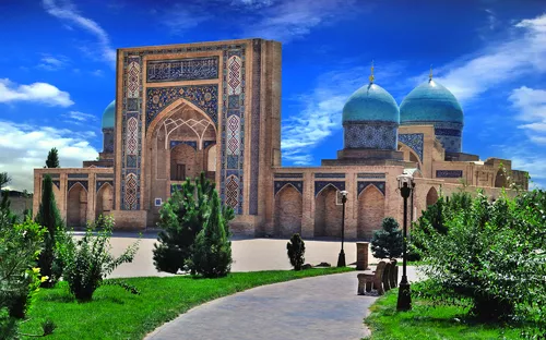 Historisches Gebäude mit blauen Kuppeln und verziertem Eingang, umgeben von Grünflächen.