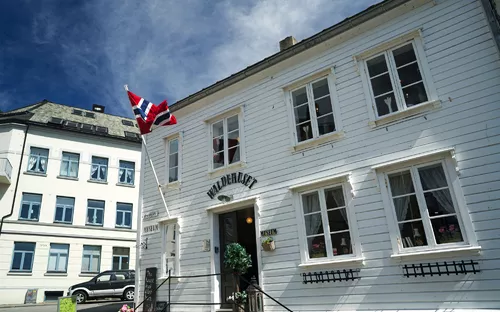 Weißes Holzgebäude mit norwegischer Flagge an der Fassade.