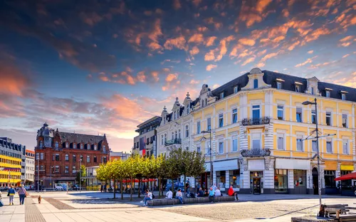 Städtischer Platz bei Sonnenuntergang mit historischen Gebäuden und Bäumen.