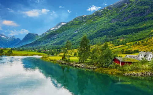 Flusslandschaft mit Bergen, grünen Wiesen, roten Häusern und blauem Himmel.