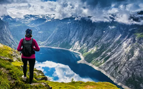 Wanderer betrachtet See und Berge unter bewölktem Himmel.