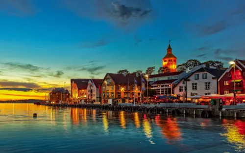 Hafenstadt bei Sonnenuntergang mit beleuchteten Gebäuden und ruhigem Wasser.