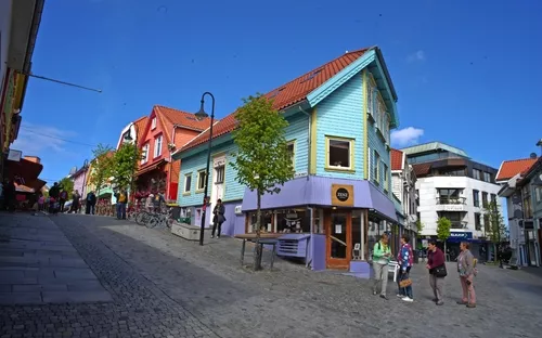 Bunt bemalte Holzhäuser in einer gepflasterten Straße mit Fußgängern an einem sonnigen Tag.