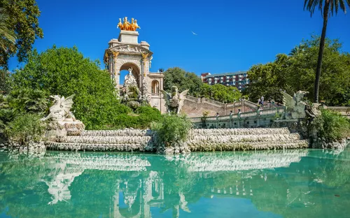 Springbrunnen und Statue in einem Park vor blauem Himmel und Palmen.