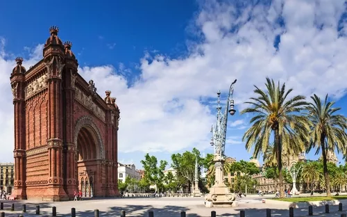 Ein roter Backsteinbogen mit Palmen im Hintergrund und einem blauen Himmel.