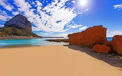 Sonniger Strand mit Felsen, blauem Himmel und Meer im Hintergrund.
