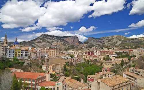 Stadtpanorama mit Bergen im Hintergrund unter blauem Himmel mit Wolken.