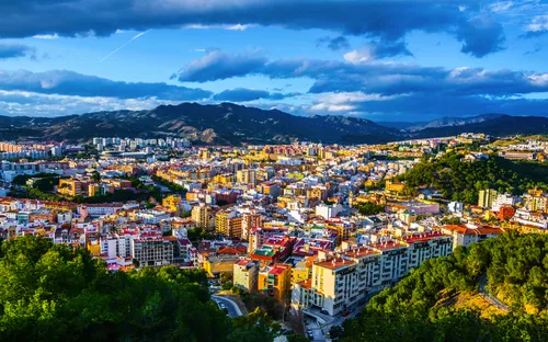 Blick auf eine Stadt mit bunten Gebäuden und Bergen im Hintergrund unter blauem Himmel.