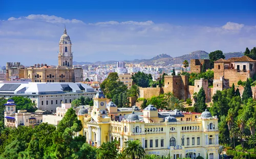 Blick auf historische Gebäude in Málaga, Spanien, umgeben von Hügeln und Vegetation.